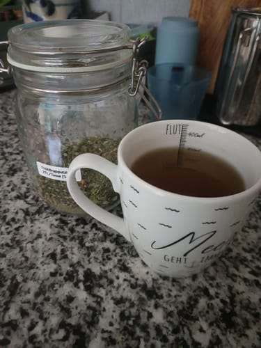 Customer's Frühlingsputz Tee mit Kräutern in einem Glasbehälter und eine Tasse fertig aufgebrühter Tee auf der Arbeitsplatte