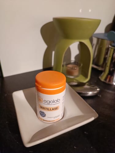 Reviewer's Mirtillase supplement bottle with an orange cap, placed on a white square dish on a dark surface.