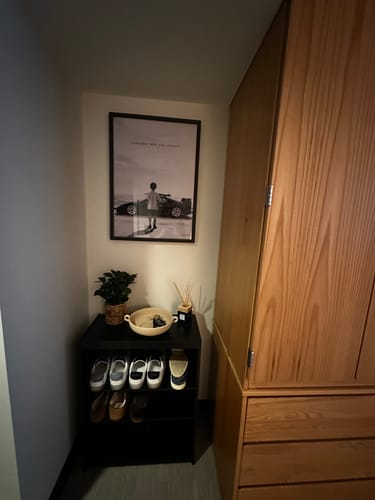 Customer's REMEMBER art print framed and hanging above a shoe rack in a dorm room.