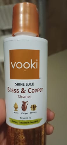 Customer's hand holding a white bottle of Vooki Shine Lock Brass and Copper Cleaner.