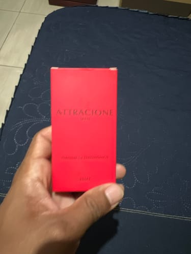 Customer's hand holding a bright red Attracione Men perfume box with black text.