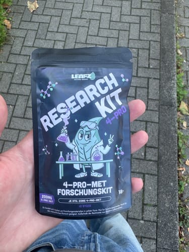 Kundenfoto der 4-Pro-MET Forschungskit-Verpackung, gehalten in einer Hand vor einem gepflasterten Gehweg.