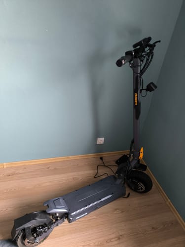 Reviewer's dark gray Ausom Gosoul 2 electric scooter standing on a wooden floor against a wall.