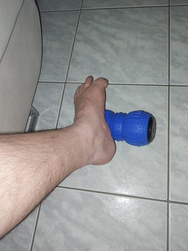 Customer's foot resting on a blue vibrating massage roller placed on a tiled floor.