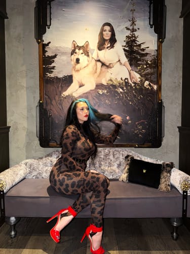 Customer's Naked Print Stirrup Jumpsuit in leopard print, worn with bright red heels while seated on a bench.