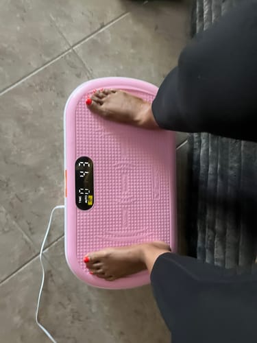 Reviewer's pink CV40 vibration plate on a tiled floor with feet placed on the textured surface.