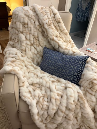 Customer's Hugs Marble Sand Blanket draped over a chair with a patterned blue pillow