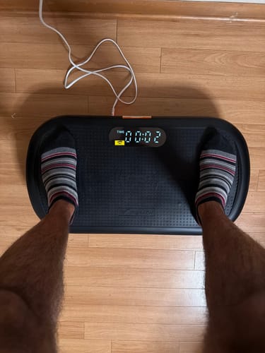 Customer's CV40 Vibration Plate, standing on the black non-slip surface with feet in striped socks, time display shows 0:02