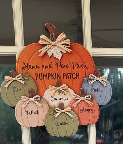 Customer's personalized pumpkin door hanger hanging on a glass door, featuring Nana and Paw Paw's Pumpkin Patch text.