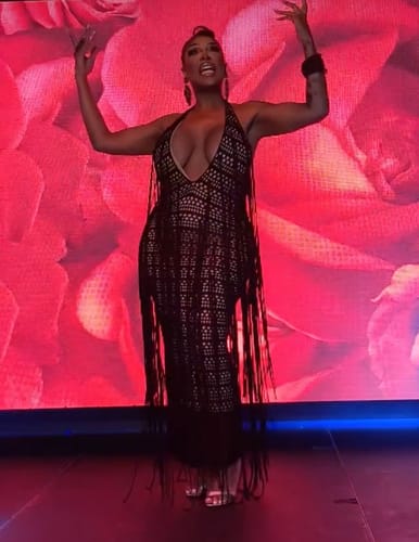 Reviewer in a black crochet maxi dress with fringe detail, posing in front of a red rose background.