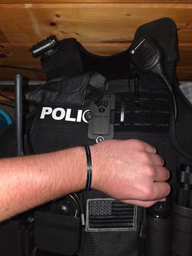 Customer's black BACK THE BLUE cuff bracelet worn on a wrist in front of a police tactical vest.