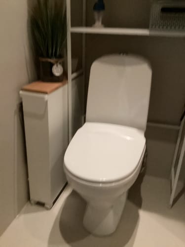 Kundens hvite oppbevaringshylle med hjul plassert i et lite baderom ved siden av toalettet.