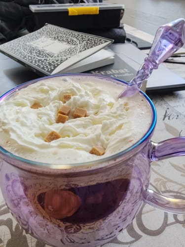 Kunden-Foto der lila Doppelwandige Hexenkessel-Tasse, gefüllt mit Sahne und Karamellstücken sowie dem passenden Löffel.