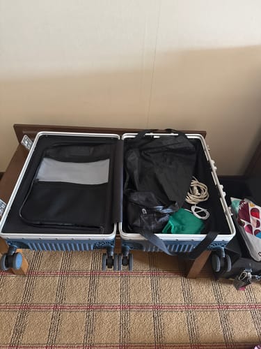 Customer's opened All-in-One Carry-On suitcase showing internal storage pockets and packed contents on a carpeted floor.