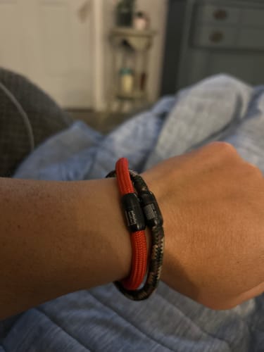 Customer's hand wearing a red paracord R.E.D. bracelet paired with a patterned camo bracelet.