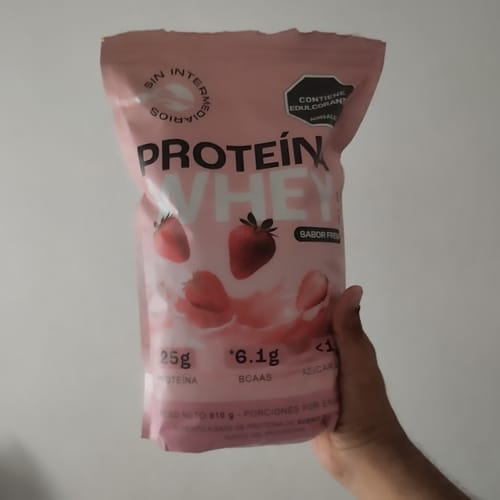 Customer's hand holding a pink Proteína Whey strawberry flavor package.