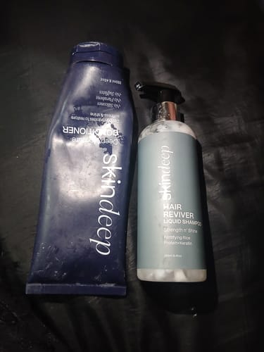 Customer's Skindeep Hair Reviver shampoo pump bottle next to a dark blue conditioner tube on a dark surface.