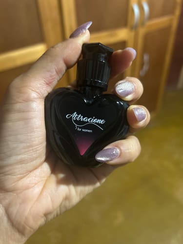 Reviewer's hand holding the heart-shaped black bottle of Perfume Attracione Sensual