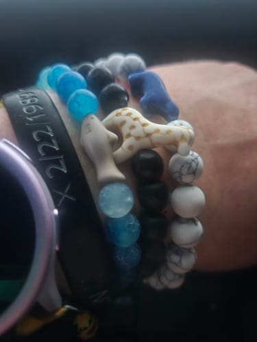 Customer's wrist wearing a Voyage Bracelet stack with colorful bead bracelets, including a shark charm