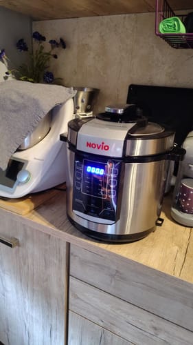 Reviewer's Novio SteelCook multicooker with digital display, placed on a wooden kitchen counter next to another appliance.