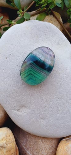 Customer's smooth Fluorine arc en ciel galet, showing blue and green banded patterns, placed on a white stone.