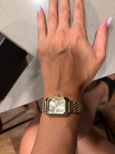 Customer's gold-toned Claire De Mains watch with a linked metal band worn on a wrist.