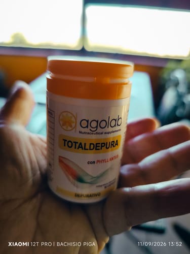 Reviewer's hand holding a white bottle of TotalDepura supplement with orange cap, close-up.