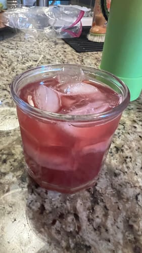 Customer's Black Currant THC Seltzer poured into a clear glass filled with ice on a stone countertop.