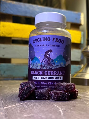 Customer's Black Currant Nighttime Gummies bottle standing in front of loose, dark, sugar-coated gummy pieces.