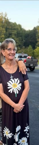 Customer standing outdoors wearing a dark floral dress, smiling for a photo.