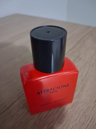 Reviewer's red Attracione Men perfume bottle with black cap sitting on a wooden surface.