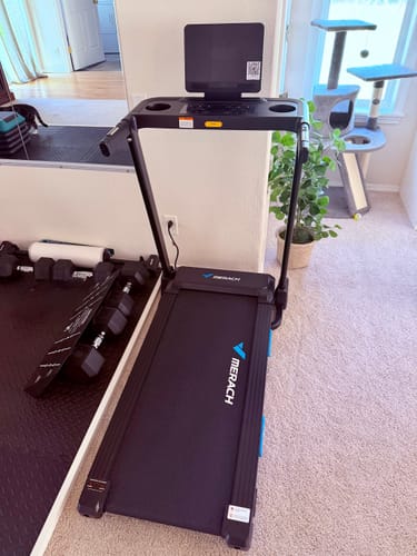 Customer's T12 Foldable Treadmill set up in a living area next to a plant and workout equipment.