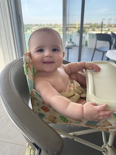 Customer's baby smiling while seated in the Sky baby chair V2 with a patterned fabric cover.