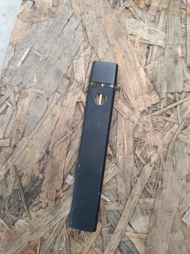Customer's black THC-A Vape pen resting on a light brown wooden surface.