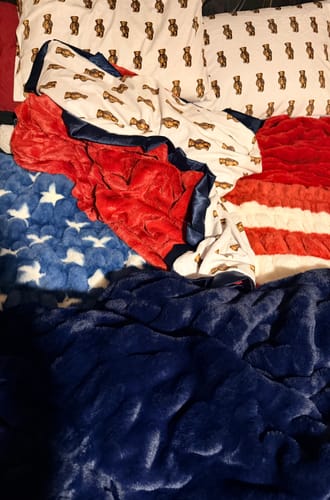 Customer's plush Hugs Navy Blanket laid over a bed with an American flag blanket and teddy bear patterned pillows