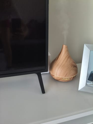 Customer's wooden grain diffuser emitting mist on a white surface next to a television.