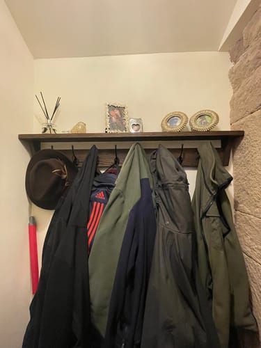 Customer's solid oak coat rack wall-mounted with multiple coats hanging on black hooks and decor items on the shelf.