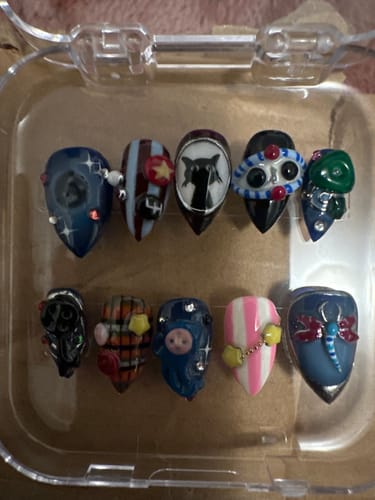 Customer's Midnight Curio press-on nails arranged in a clear plastic case, featuring detailed charms and nail art.