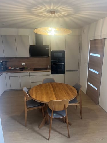 Customer's NEO teinté Chêne suspension, en bois clair, installée au-dessus d'une table ronde dans une cuisine moderne.