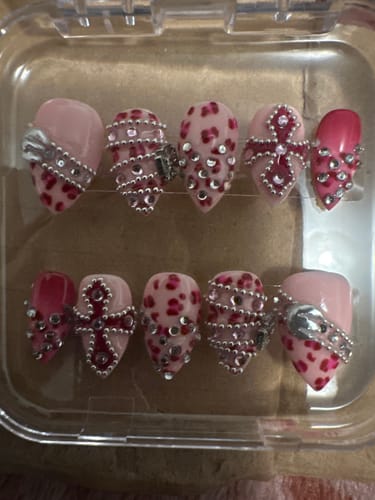 Customer's Pink Venom nail set in plastic case, featuring pink leopard print, rhinestones, and cross motifs.