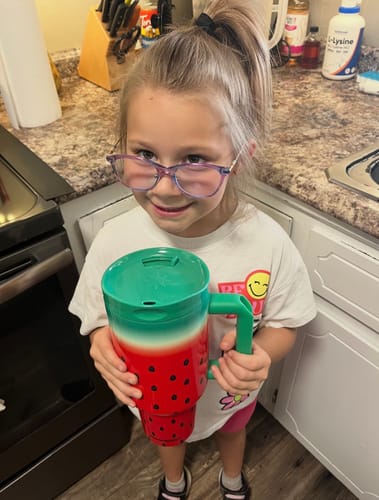 Customer's child holding a Watermelon Kiss Thicc Buddy 50oz mug in a kitchen.