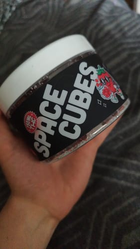Kundenhand hält den schwarzen Behälter der THC Space Cubes mit weißem Deckel und Logo-Etikett.
