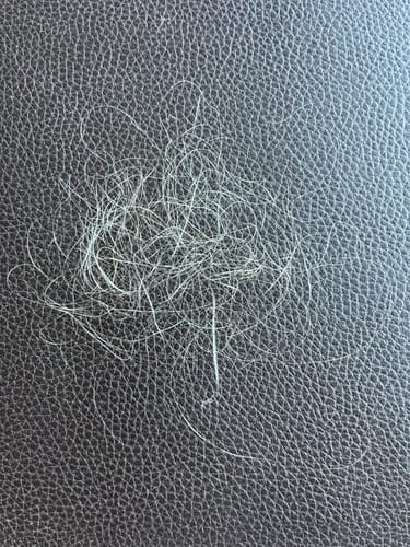 Customer's Kérastase Genesis Serum results showing a small tangle of fallen hair on a dark textured surface.