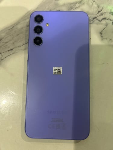 Customer's purple Samsung Galaxy A34 5G smartphone showing the triple camera layout on a marble surface.