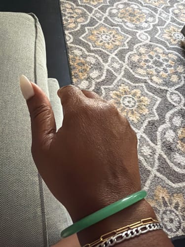 Customer's hand wearing the green AMALI Bangle stacked with other gold and silver bracelets.