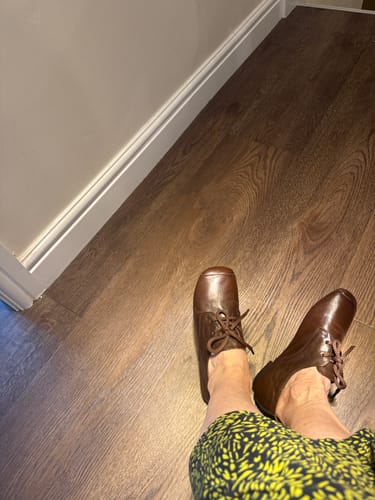 Customer's brown square-toe shoes worn on feet while standing on a wooden floor