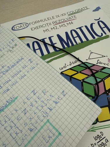Reviewer's Carte Matematică Bacalaureat book next to a handwritten notebook containing math notes and formulas.