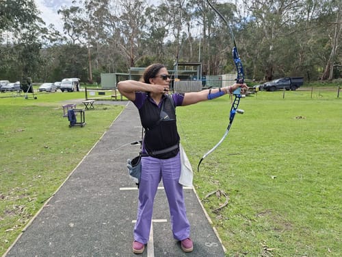 Reviewer wearing purple Construction Pants while practicing archery on a grassy field.