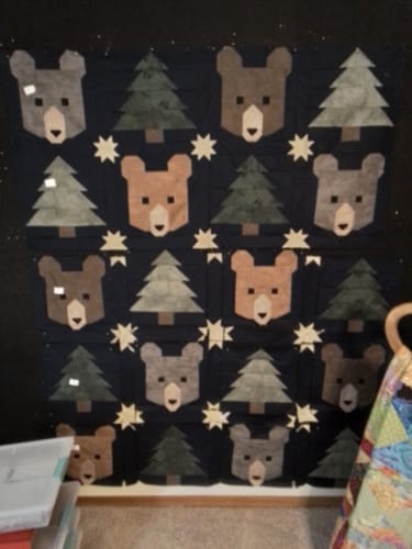 Customer's Midnight Pines quilt in progress on a wall, featuring bear and pine tree blocks on a dark background.