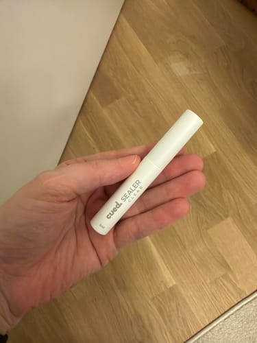 Kundenfoto des weißen Cued Sealer Stifts, gehalten in einer Hand über einem Holzboden.